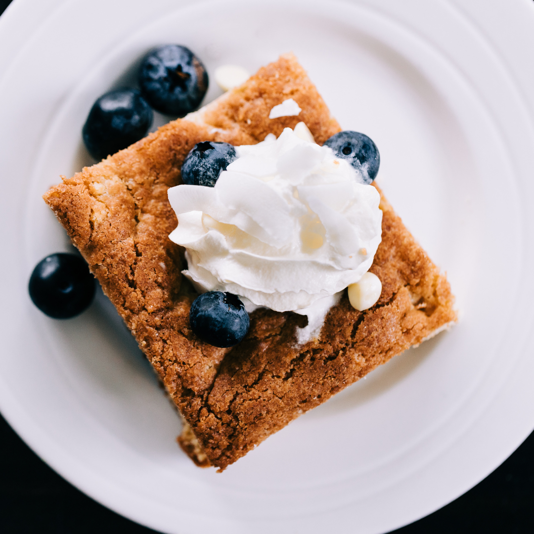 A slice of Secret Kiwi Kitchen blondie with blueberries and whipped cream