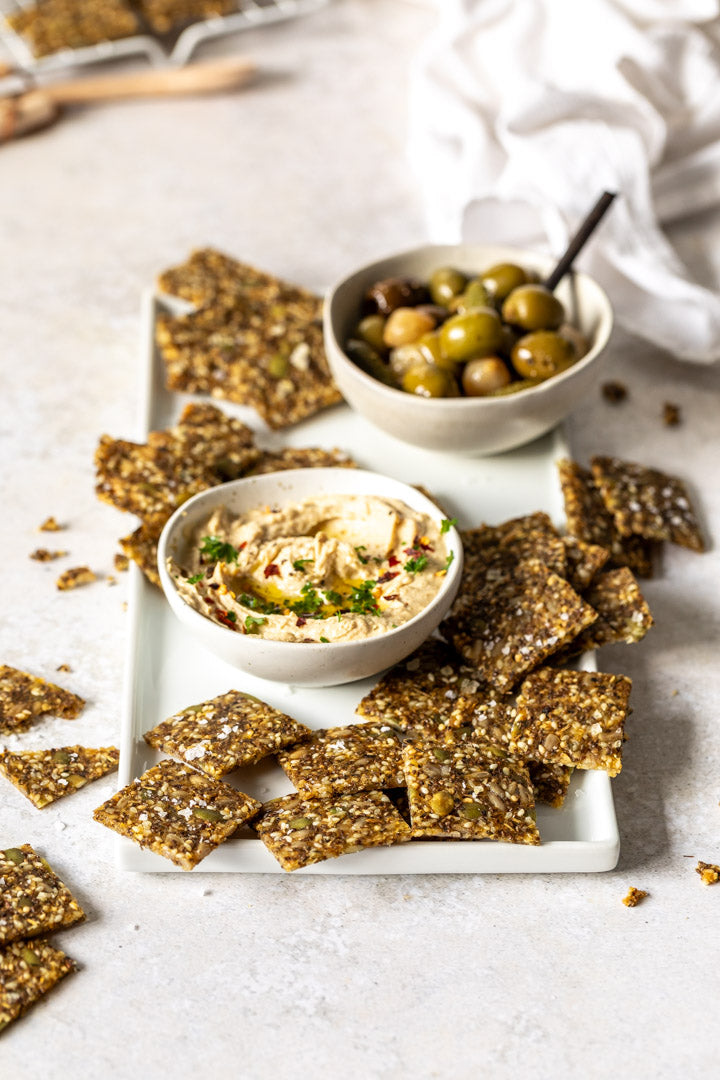 Secret Kiwi Kitchen Seeded Cracker snacks with hummus and olives on a white plate