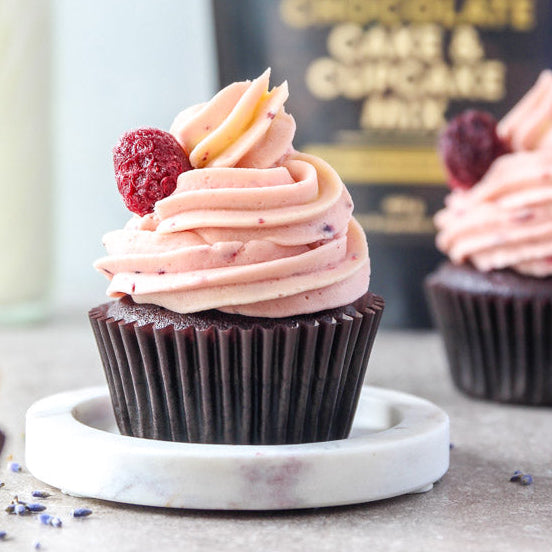 Close-up of a chocolate cupcake with raspberry icing and a raspberry with bag of Cake & Cupcake mix behind.